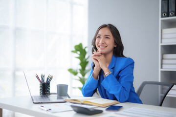 Obraz premium Successful Asian businesswoman smiling using laptop and computer at office. Confident Asia businesswoman sitting happily in the office.