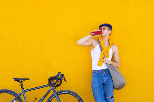 a man drinks water from a thermo mug leaning on a bicycle
