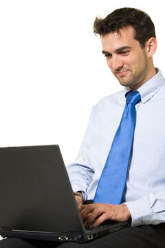 Attractive brunette business man sitting while working on a laptop computer wearing blue shirt and tie