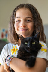 Portrait of little girl with cute black cat with green eyes. Girl hugging hers cute long-haired kitten of hers. Background, copy space, close up. Adorable domestic pet concept.