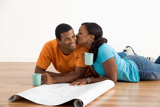 African American female kissing man next to blueprints.