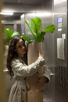 girl rides in an elevator with a flowerpot