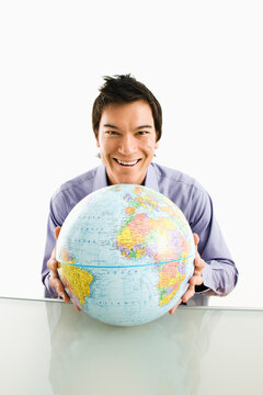 Young Asian man sitting holding globe smiling.