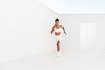 Woman runner in white fitness clothes. Full length on fitness influencer sprinting.