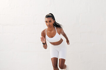 Fototapeta na wymiar Young slim female athlete running outdoors against a white wall. Fitness influencer in white sportswear sprinting.