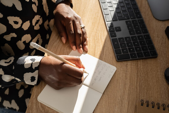 Faceless black woman taking notes in copybook