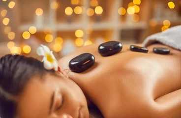 Keuken foto achterwand Spa Young woman getting hot stone massage in spa salon. Close up shot of attractive young woman lying with closed eyes enjoying massage and spa. Beauty treatment, wellness, body care concept