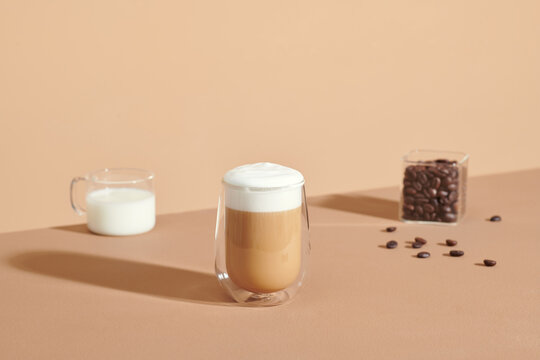 Glass cup of tasty latte, coffee beans and jug with milk on