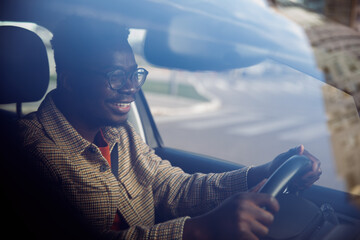 Smiling young man driving a car seen through the window glass.