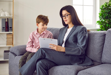 Woman child psychologist working with little boy at her office. smiling little boy during meeting. Cute boy preschooler and friendly counselor sitting on sofa in office and communicating