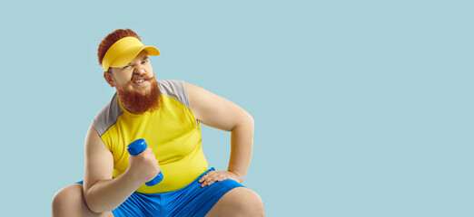 Funny bearded plump fat man in yellow sun visor sitting isolated on blue text copyspace banner background, doing sports exercise and pretending that dumbbell is heavy. Studio shot. Gym workout concept - obrazy, fototapety, plakaty