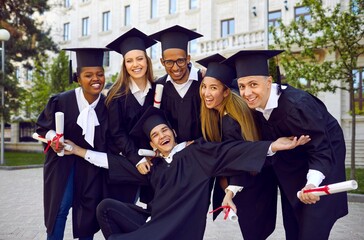 Group of happy smiling multicultural people in graduation gowns and caps with diplomas in hands...