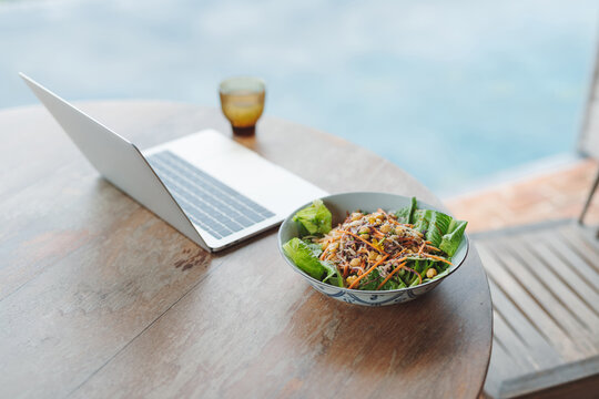 horizontal of computer on wooden table near bowl of tasty breakfast
