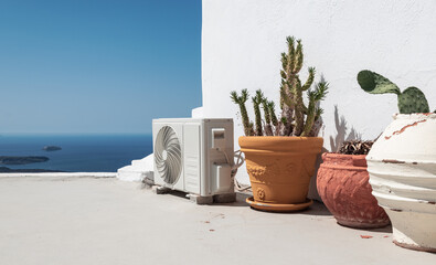 Air conditioning or heat pump unit near potted plants in Santorini, Greece.