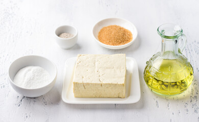 Ingredients for vegan syrniki, tofniki: tofu, rice flour, brown sugar and vanilla sugar on a light blue background. Cooking delicious healthy food