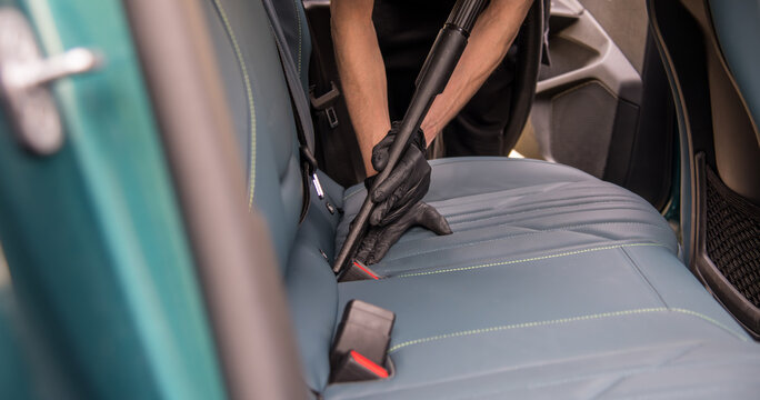Ein Mann mit Handschuhen saugtAuto mit Lederausstattung aus	
