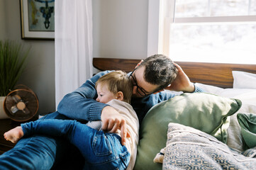 young dad hugging and holding his son while they lay in bed at home