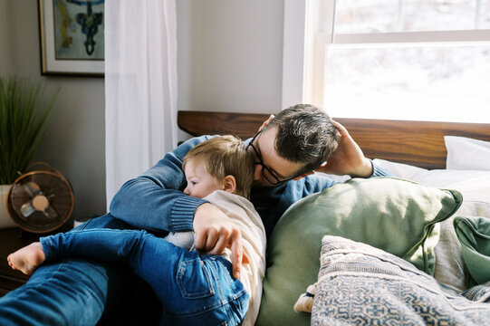 young dad hugging and holding his son while they lay in bed at home
