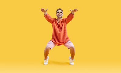Fototapeta na wymiar Full body photo of a cool funny young man with unshaven beard wearing bright casual clothes and white sneakers having fun doing sport exercise isolated on a studio yellow background. Banner.
