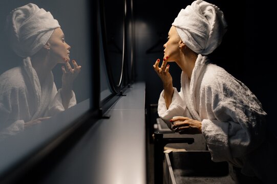 Woman in bathrobe applying cream on face in bathroom
