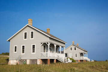Low angle view of two identical looking beachfront homes against a backdrop of a clear, blue sky....