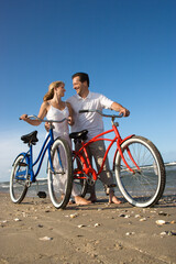 Obraz premium Man and woman look at each other while pushing bikes on the beach. Vertical shot.