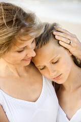 Daughter rests her head on her mother's shoulder at the beach. Vertical shot.