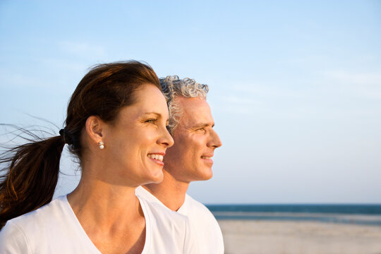 Side view of smiling middle aged couple on beach looking off into the distance together. Horizontal shot.