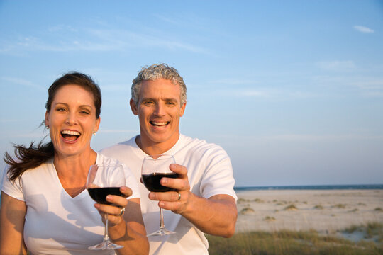 Happy couple drink wine on the beach and raise their glasses to the camera. Horizontal shot.