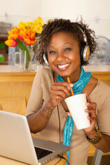 A young woman sitting in a cafe and drinking a beverage. She has a laptop open on the table in...