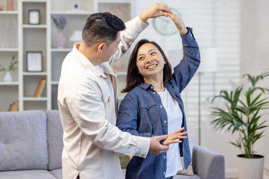 Happy Asian couple, young family man and woman celebrate moving to a new house, buying an apartment. They dance, hug, laugh.