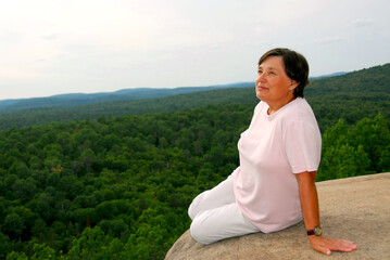 Fototapeta na wymiar Mature woman sitting on cliff edge enjoying scenery