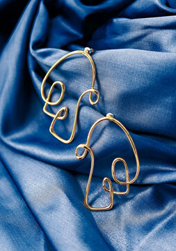 Unique Gold Earring Against Blue Satin Fabric