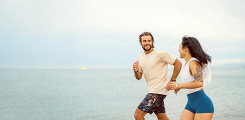 Cheerful young multi-ethnic couple running on the sandy sea beach wearing summer sport clothing