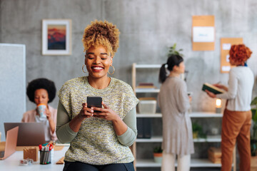 African-American woman smiling while texting over phone in startup company office.