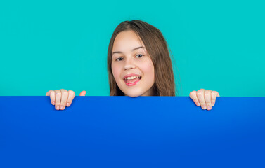 cheerful kid behind blank blue paper with copy space for advertisement
