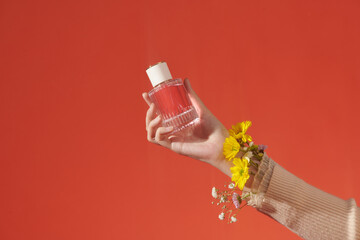 Perfume bottle in a female hand on a red background.