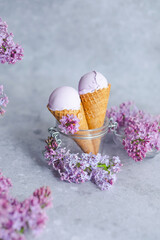 Purple ube extract ice cream in cones decorated with lilac flowers on a gray background. Filipino ice cream. Healthy vegan dessert