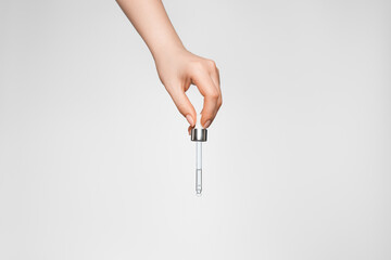 Female hand on a light background with a pipette.