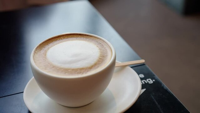 4k rotate video, Fresh hot latte in ceramic white cup with smoke in cafe or restaurant .beverage morning concept. drink of coffee with creamy milk on old wooden plate