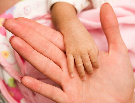Tiny newborn baby hand against and adult female hand to show how small the hand is up close