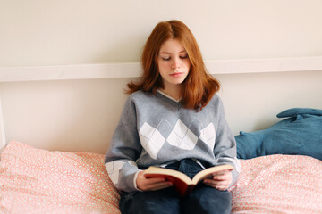 The girl sits on the sofa and reading a book. Student or schoolgirl on distance learning. Home work concept. Relaxation.