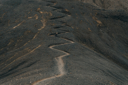 Hiker man on curved gravel zigzag hiking trail of volcanic mountains