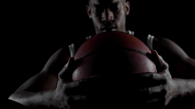 Basketball player sitting on a bench. Concentrated african american sports man against black background.