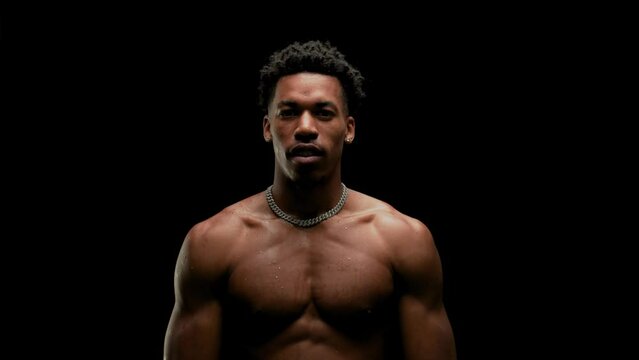 Muscular man showing muscles. African American male posing against black background.