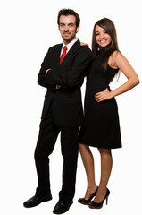 Full body of an attractive brunette woman wearing black formal dress and man in suit and red tie standing beside each other over white