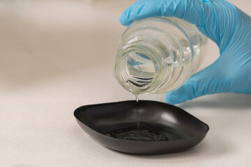 Close up of a hand of a lab technician with blue nitril gloves pouring liquid into a black plastic container in a scientific laboratory. background. Science, analyse, analysing, DNA analysis