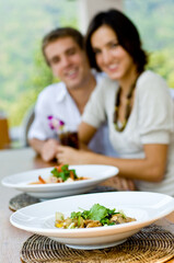 A young couple on vacation eating lunch at a relaxed outdoor restaurant (focus on food)