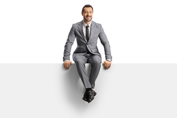 Full length portrait of a businessman in a grey suit sitting on a blank panel and smiling