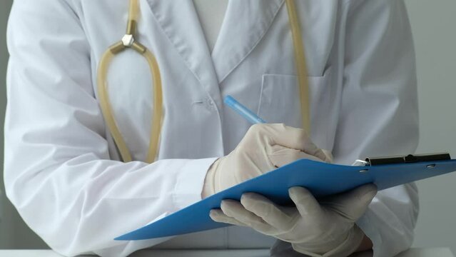 Female doctor filling up medical form at clipboard in hospital, close up. Physician with stethoscope holding notebook in hand. Health care, medicine concept